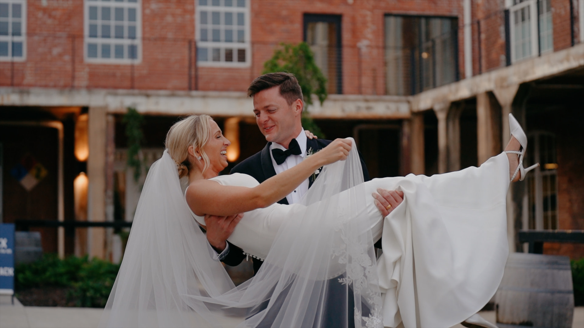 Groom carrying his laughing bride outside a brick venue courtyard